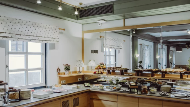 Frühstücksbuffet in einem Hotel mit Spiegelwand und Fenstern.