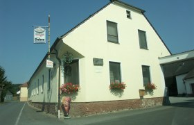 Ein gelbes Gasthaus mit Blumen und Eistafel an einer Landstraße.
