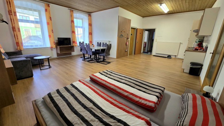 Interior view of a spacious apartment with wooden floor, double bed, dining table, sofa and TV.