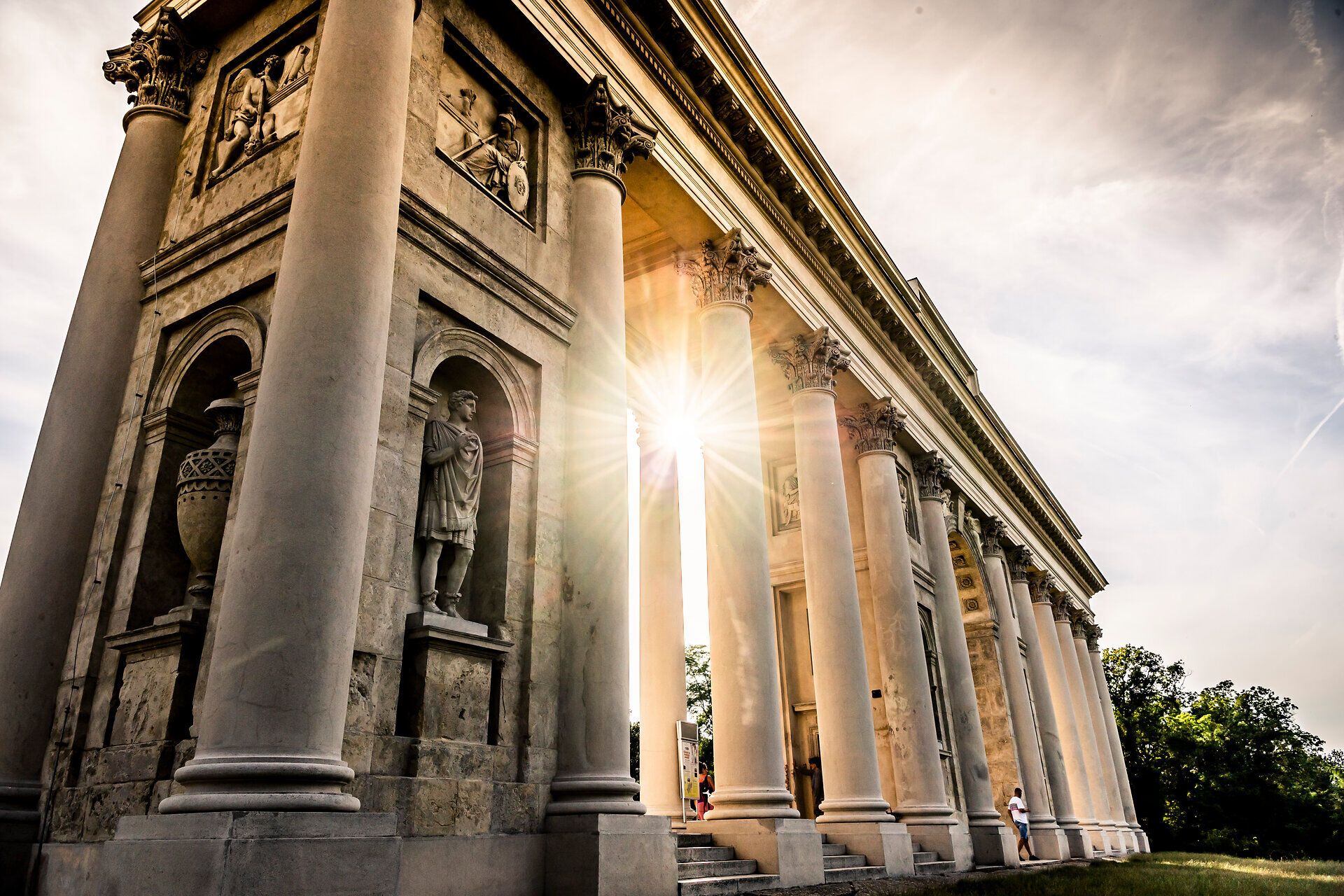 Die majestätische Raistenkollonade strahlt im warmen Licht der Abendsonne und lädt dazu ein, die beeindruckende Architektur zu bewundern. Umgeben von üppigem Grün und sanften Hügeln, bietet dieser Ort eine perfekte Kulisse für entspannte Spaziergänge und unvergessliche Erinnerungen.
