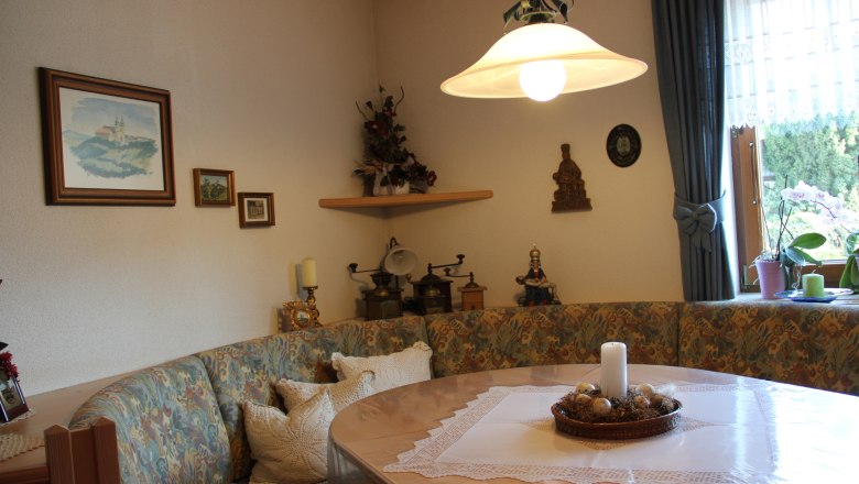 Gemütlicher Frühstücksraum mit Eckbank, Tisch, Kerze und Dekorationen an der Wand.