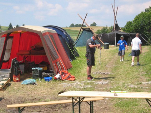 Menschen auf einem Zeltplatz mit verschiedenen Zelten und Campingausrüstung.