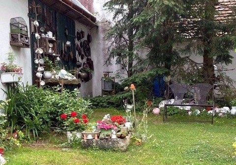 Ein Garten mit alten Töpfen und Dekorationen an einer Wand, Blumenbeet und zwei Stühlen.
