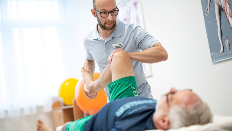 Ein Physiotherapeut behandelt das Bein eines liegenden Patienten in einem Behandlungsraum.