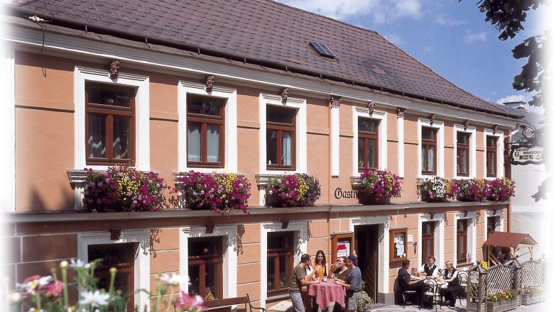 Ein traditionelles Gasthaus mit blumengeschmückter Fassade und Gästen, die draußen an Tischen sitzen.