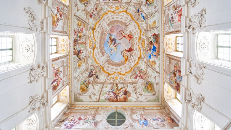 Zwei Personen betrachten die kunstvoll bemalte Decke eines barocken Treppenhauses im Stift Altenburg.