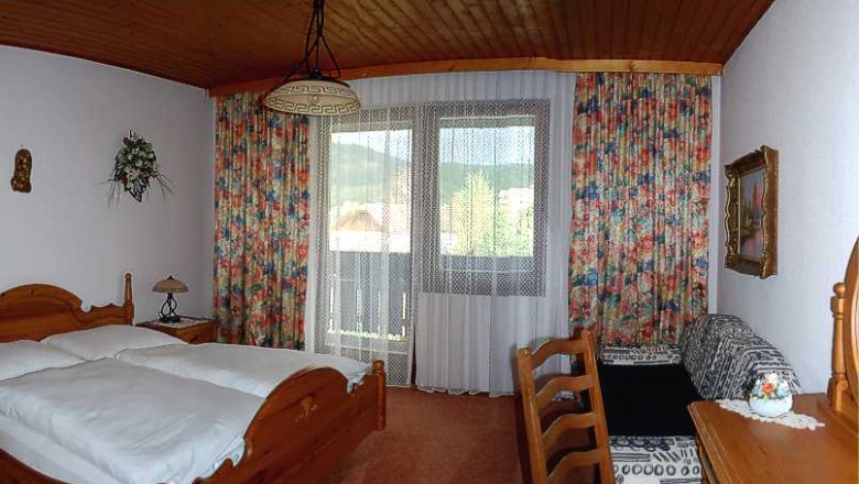 Gem&uuml;tliches Hotelzimmer mit Holzm&ouml;beln, Doppelbett, Balkon und bunten Vorh&auml;ngen.