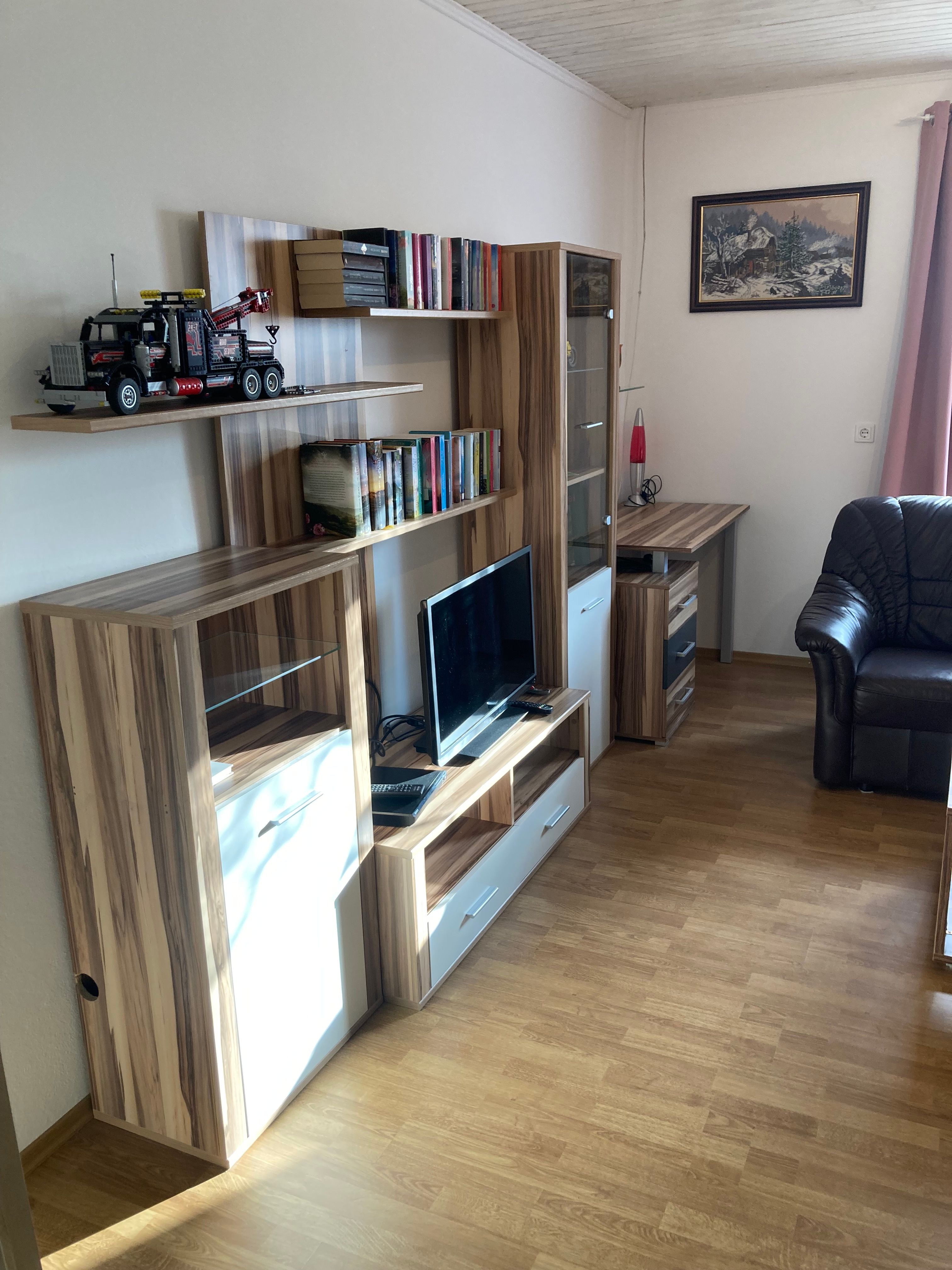 Wohnzimmer mit Holzwohnwand, Fernseher, Bücherregal und Modellauto.
