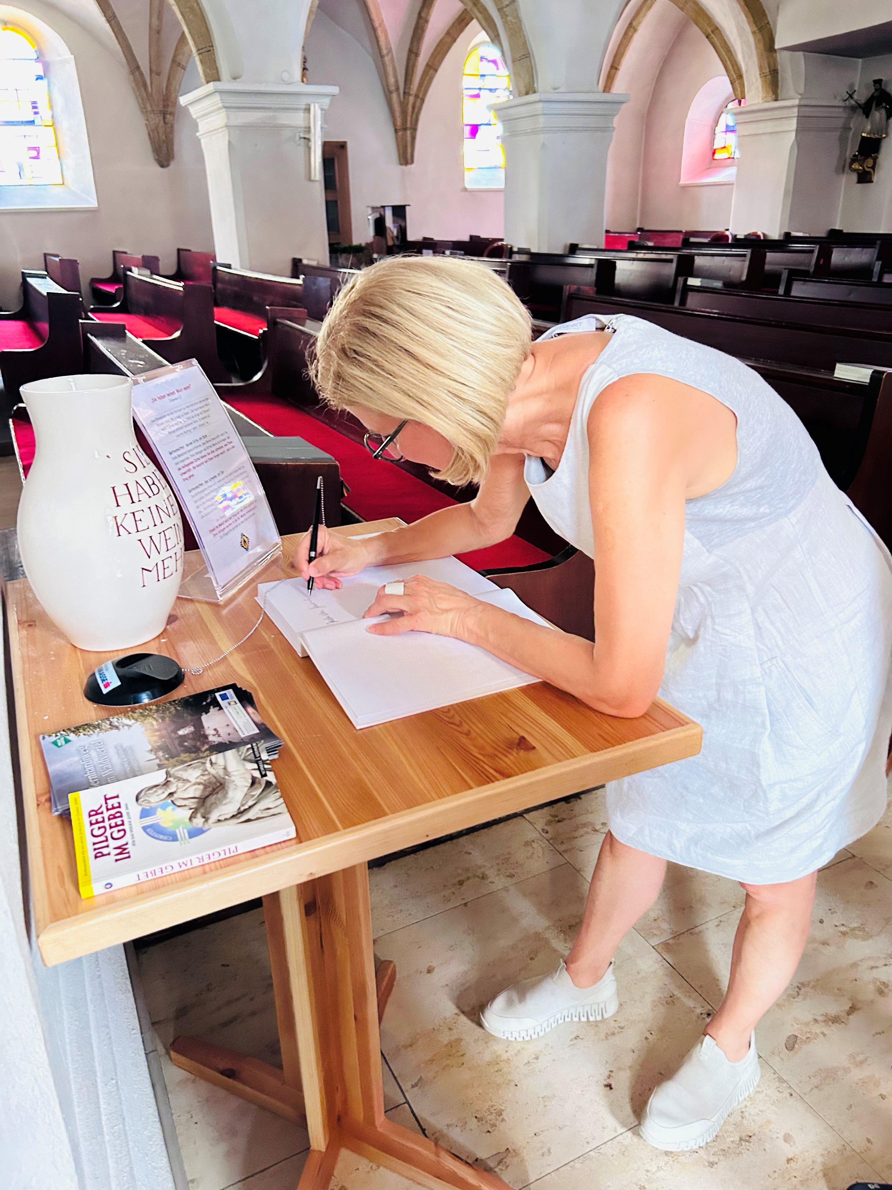 Pilgerbuch auf einem Tisch. Landeshauptfrau schreibt in das Pilgerbuch.