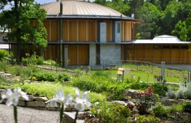 Rundes Geb&auml;ude mit Holzw&auml;nden und Garten im Vordergrund.