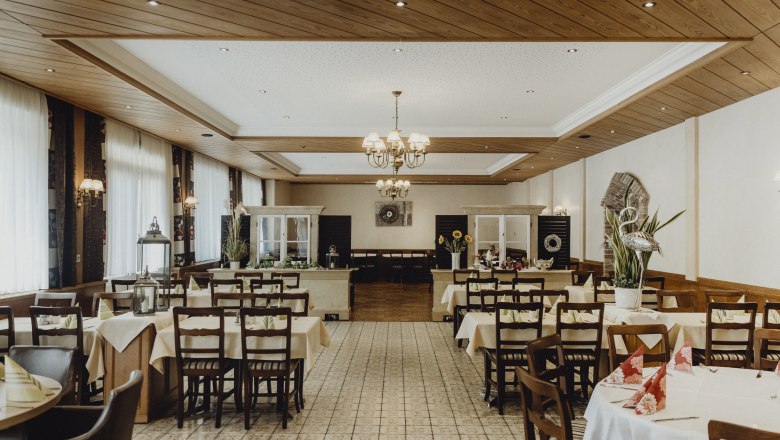 Innenansicht eines traditionellen Wirtshauses mit gedeckten Tischen und Holzdecke.