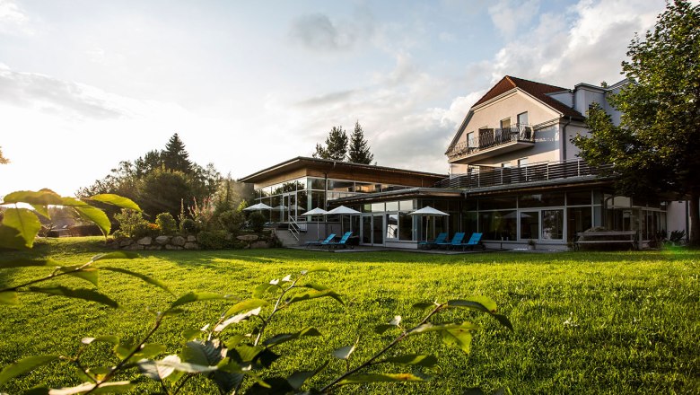 Ein modernes Gebäude mit großen Fenstern und Liegestühlen auf einer grünen Wiese bei Sonnenuntergang.