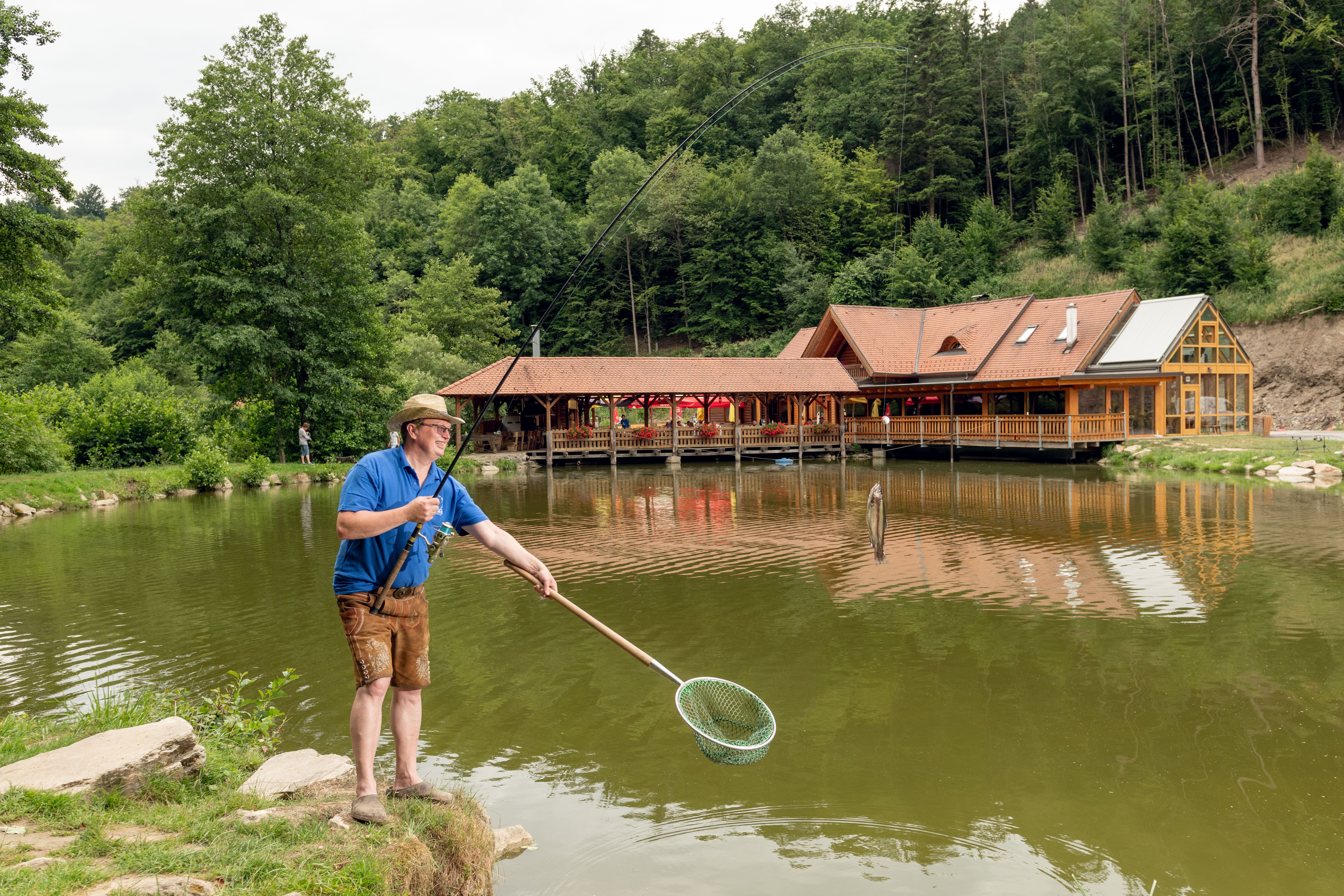 Ein Mann beim Fischen am See mit einer Angel in der Hand und einem Fisch.