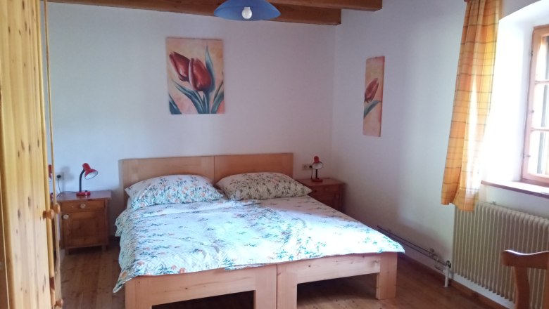 Gemütliches Schlafzimmer mit Holzbett, Nachttischen und Blumenbildern an der Wand.