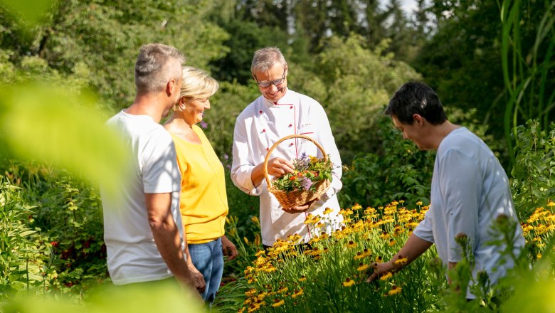 Vier Personen in einem Kräutergarten, eine Person hält einen Korb mit Kräutern.