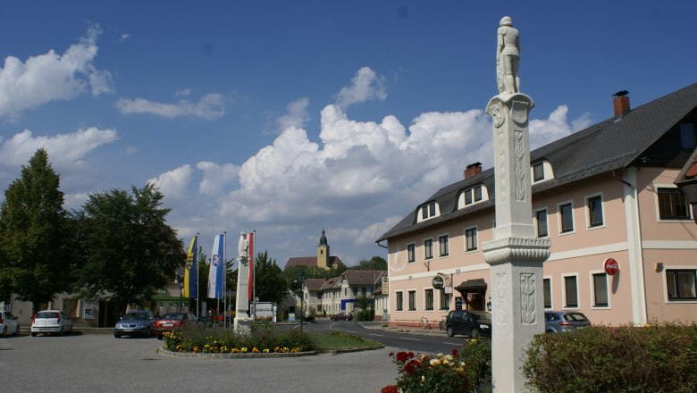 Ein Platz in Weitersfeld mit einer Statue, mehreren Flaggen und einem Gebäude im Hintergrund.