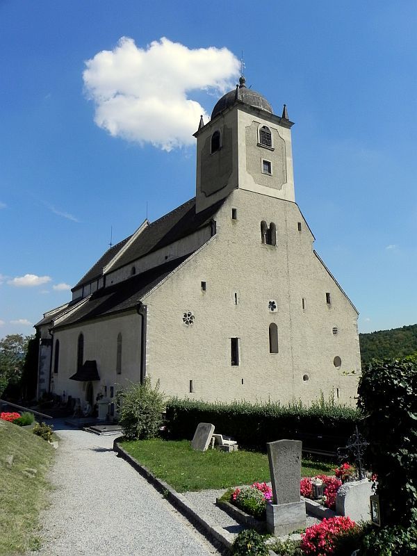 Eine historische Kirche mit einem Turm und umliegendem Friedhof bei klarem Himmel.