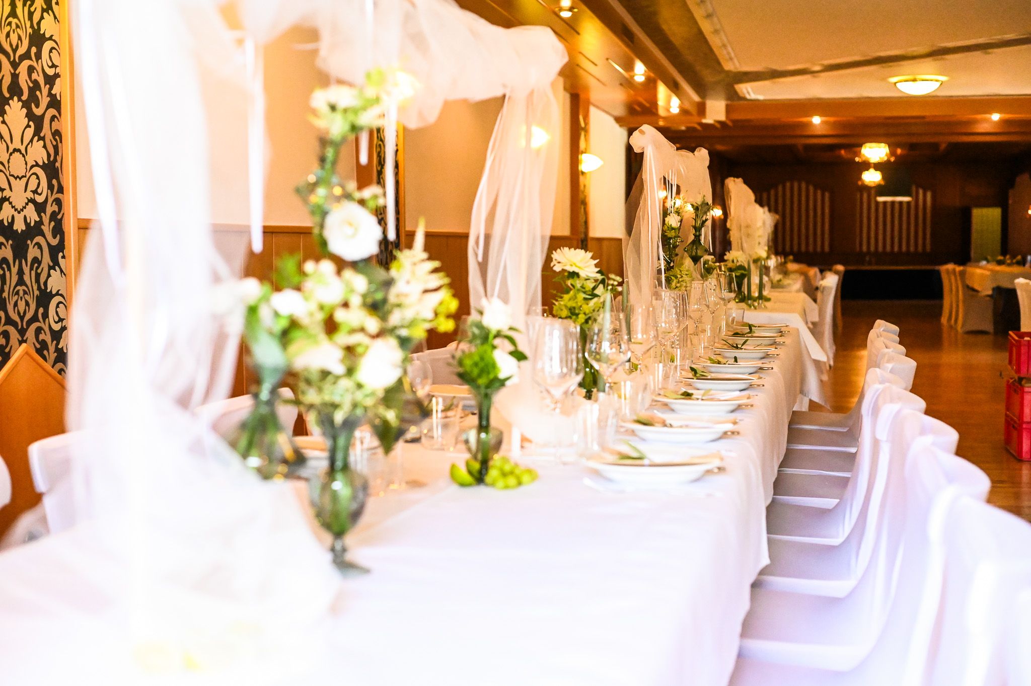 Eleganter Hochzeitstisch mit weißen Tischdecken, Blumenarrangements und Weingläsern in einem festlich dekorierten Raum.