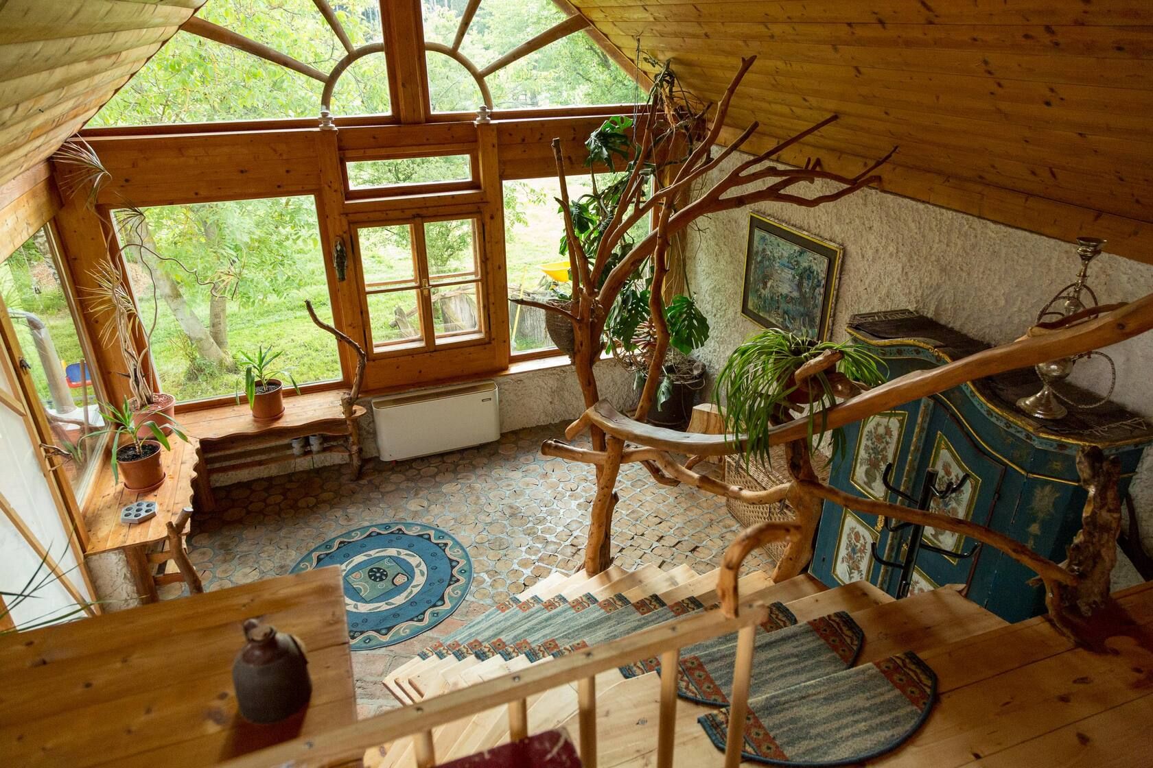 Holzinterieur mit Treppe, großen Fenstern, Pflanzen und rustikaler Dekoration in einem hellen Raum.