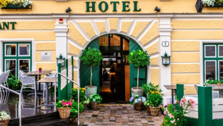 Eingang eines gelben Hotels mit Pflanzen und Sitzbereich.