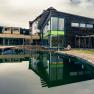 Modernes Wellnesshotel mit Holzfassade und großem Teich im Vordergrund.