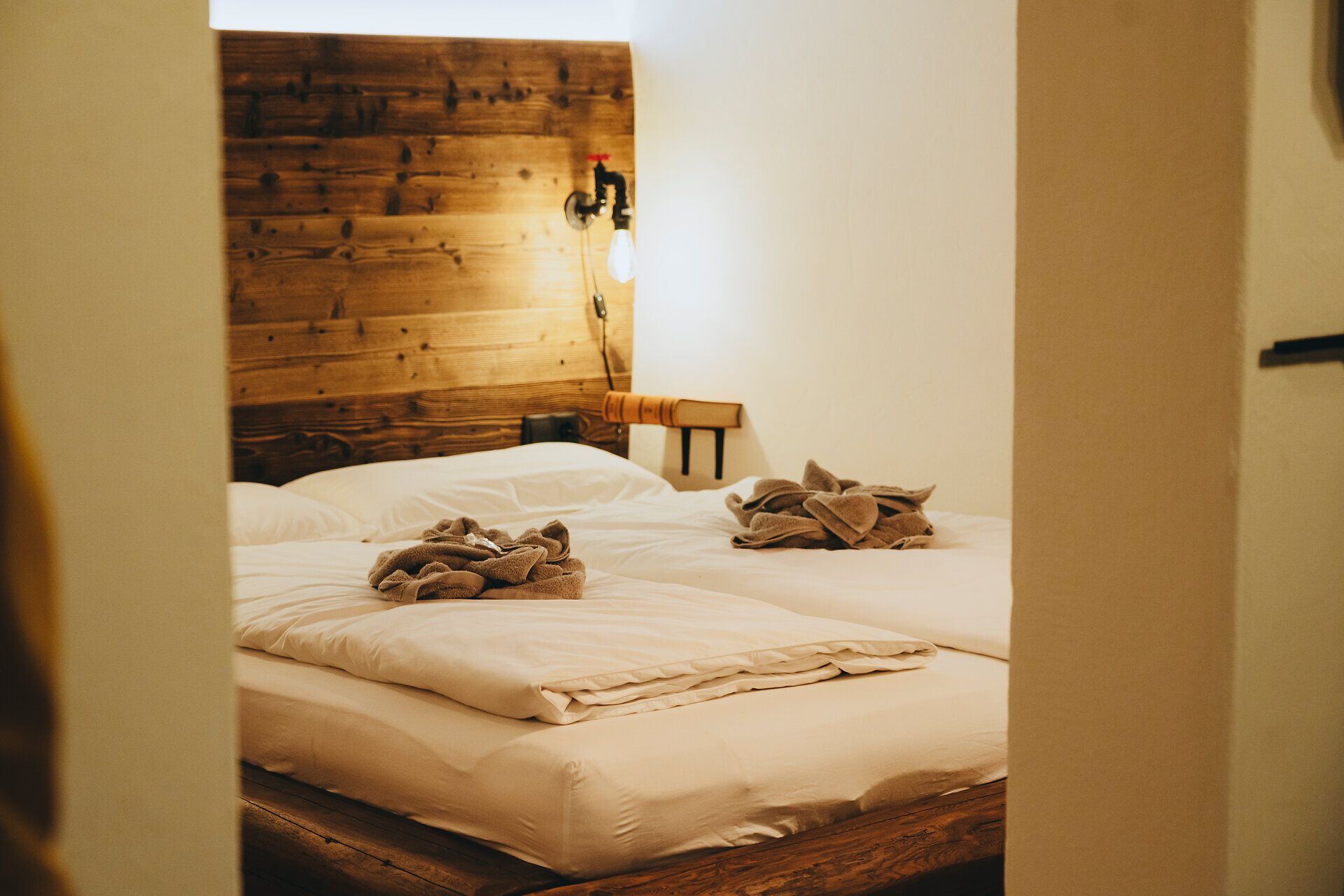 In einem gemütlichen Raum mit warmen Holztönen und sanfter Beleuchtung laden zwei Betten zum Entspannen ein. Die sorgfältig gefalteten Handtücher auf den Betten verleihen dem Raum eine einladende Note, ideal für eine erholsame Auszeit in der Natur.