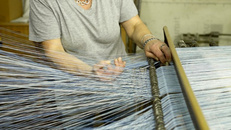Person working on a loom with blue threads.
