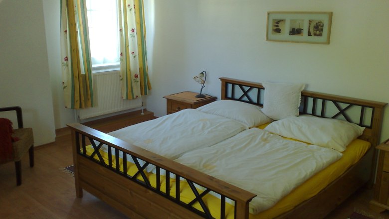Schlafzimmer mit Doppelbett, gelber Bettwäsche, Holzmöbeln und Blumenvorhängen.