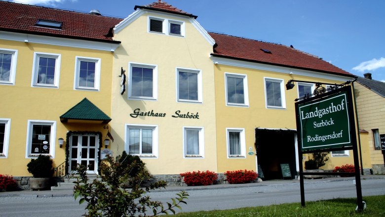 Landgasthof Surböck, © Landgasthof Surböck Gelbes Gebäude mit der Aufschrift 'Gasthaus Surböck' und einem grünen Schild 'Landgasthof Surböck Rodingersdorf'.