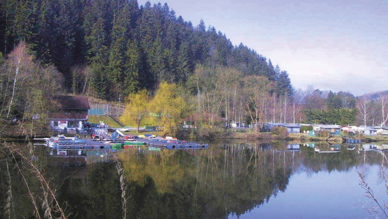 Seecampingplatz mit Wohnwagen und Booten am Ufer eines Sees, umgeben von Wald.