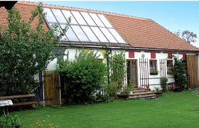 Ein traditionelles Gebäude mit Solarpanelen auf dem Dach und einem gepflegten Garten davor.