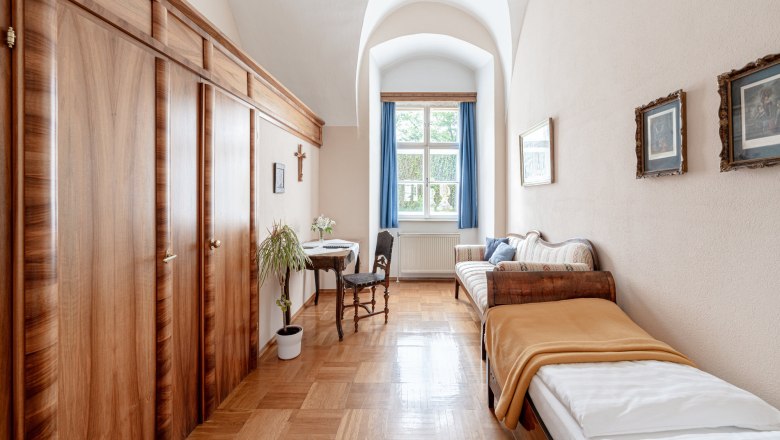 Ein traditionell eingerichtetes Doppelzimmer mit zwei Einzelbetten, Holzmöbeln und einem Fenster mit blauen Vorhängen.