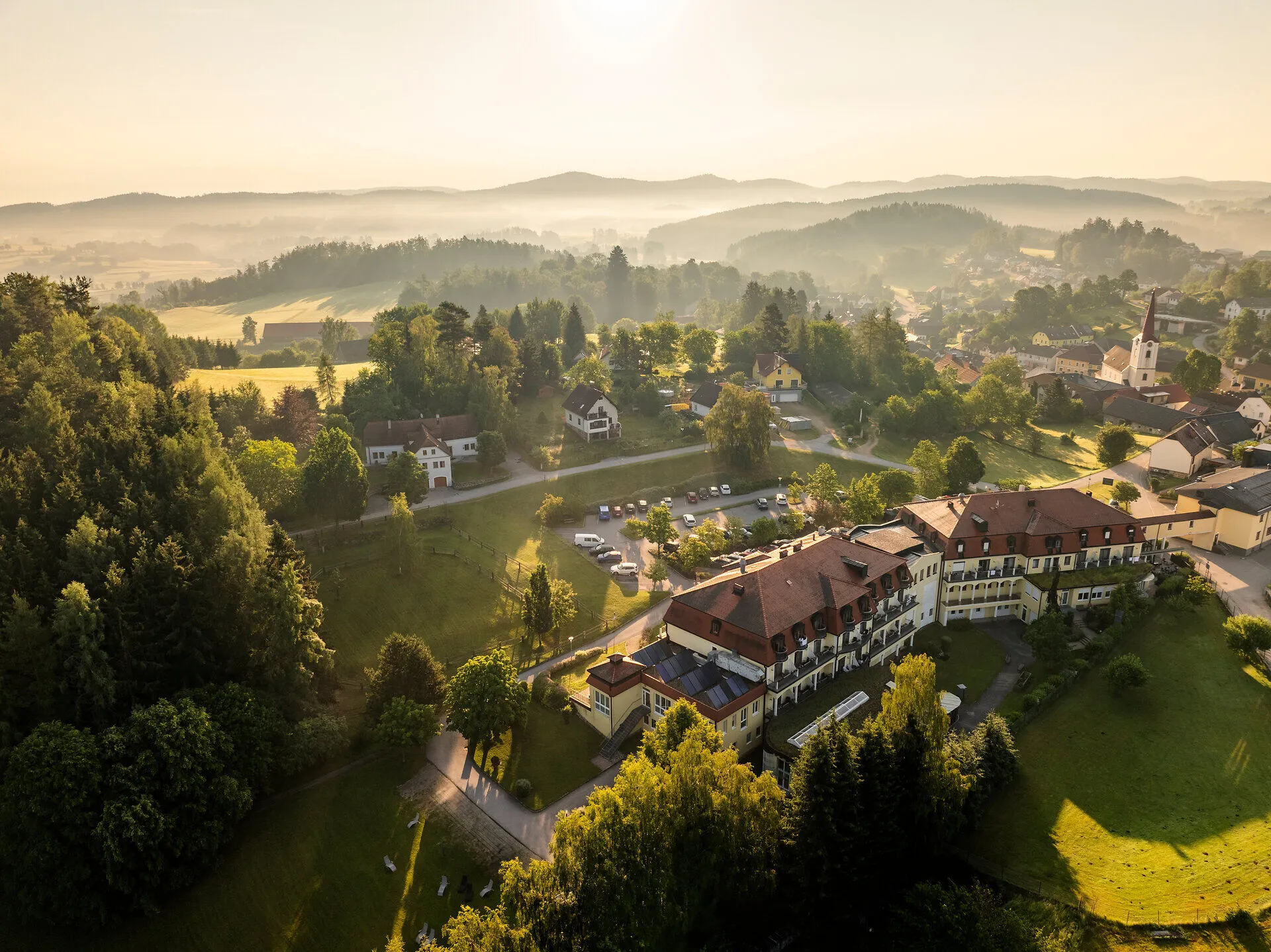 Luftaufnahme des Moorbads Bad Großpertholz im Waldviertel mit umliegendem Ort, Wiesen und bewaldeten Hügeln.