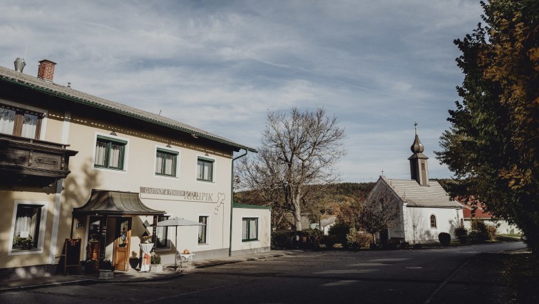 Gasthof und Kirche in Steinbach bei Nagelberg, umgeben von Bäumen und blauem Himmel.