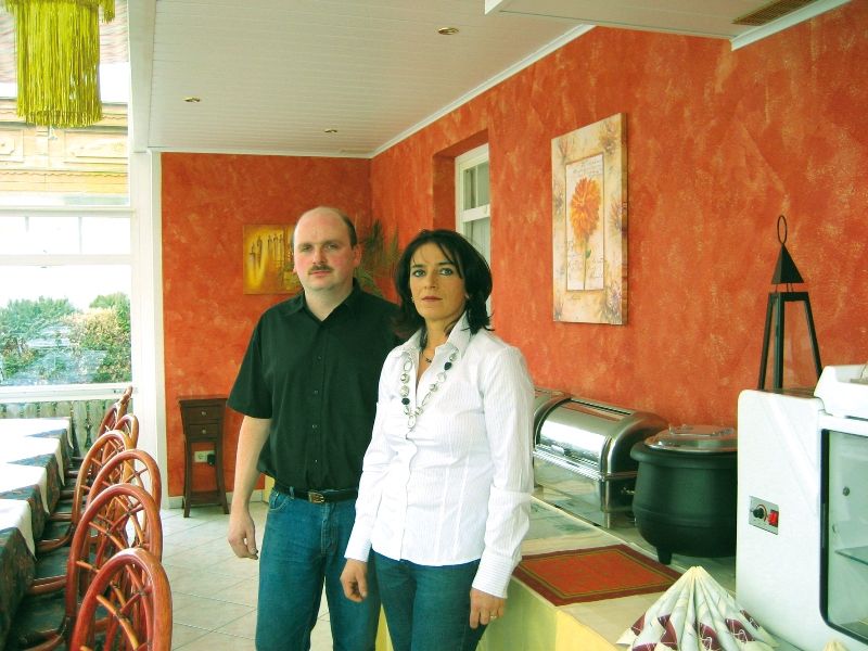 Zwei Personen stehen in einem Restaurant mit orange gestrichenen Wänden.