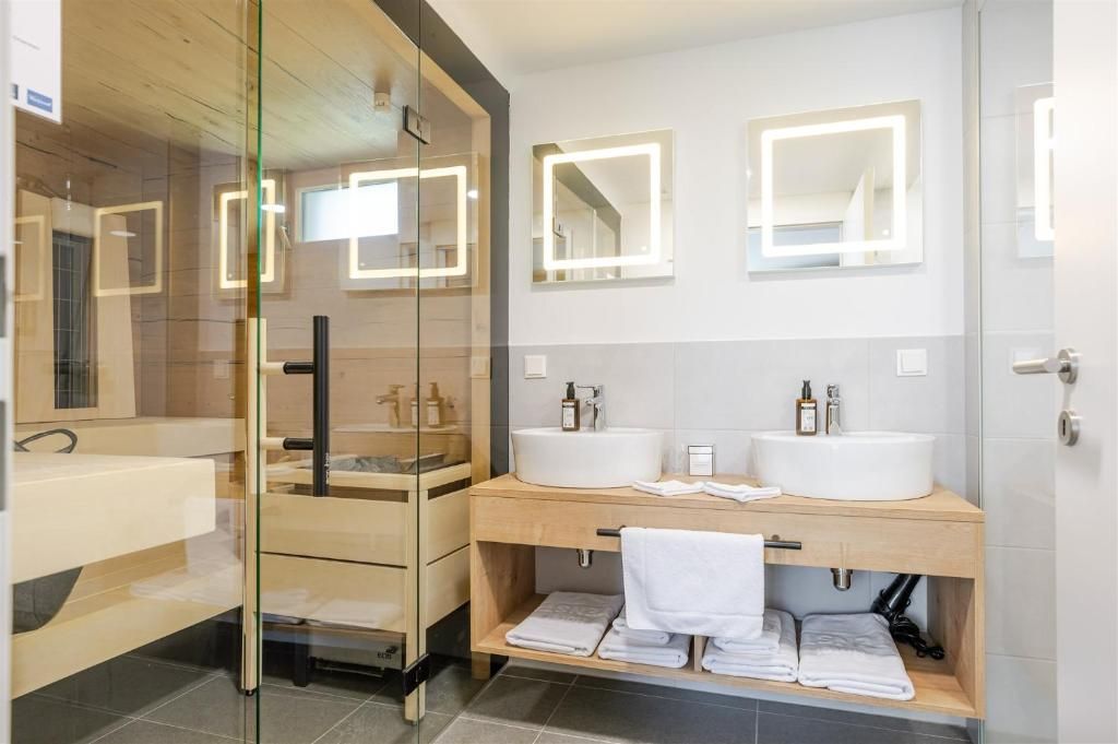 Modernes Hotelbad im Hotel Ottenstein – Das Wohlfühlhotel mit Doppelwaschbecken, Spiegeln und Glasdusche.