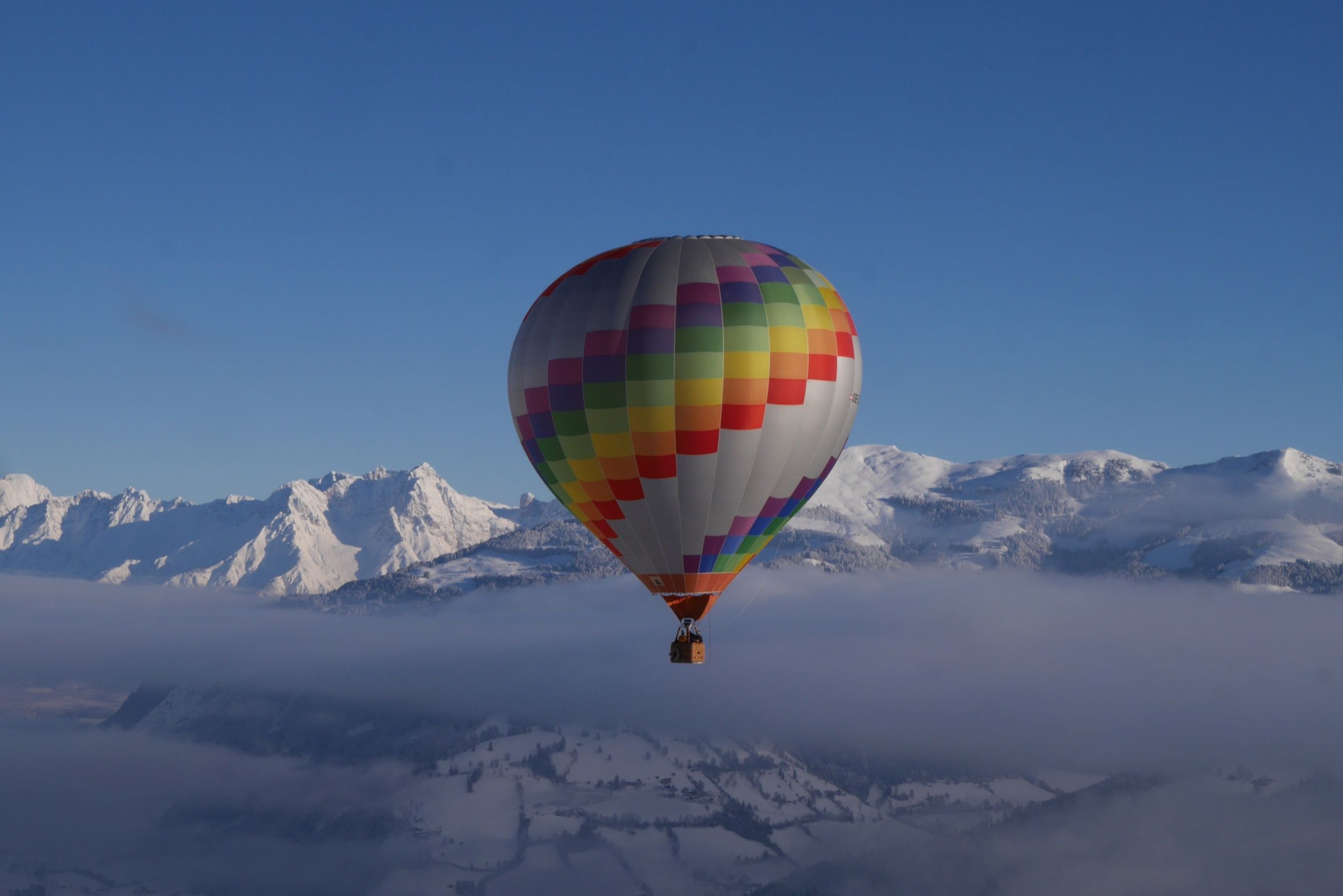 Heißluftballon über schneebedeckten Bergen und Wolken.