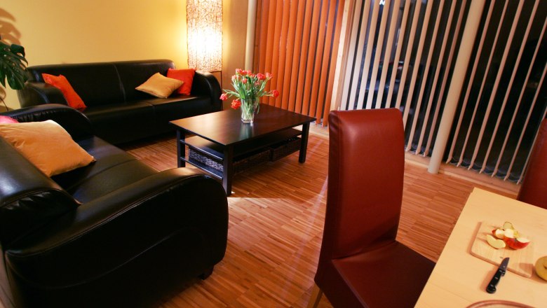 Gemütliches Wohnzimmer mit Ledersofas, Couchtisch, Blumenstrauß und Esstisch mit Obst.