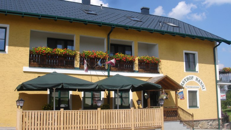 Gelbes Gebäude mit Balkon, Blumen und Terrasse mit Sonnenschirmen.