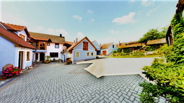 Courtyard with several buildings, blue sky, paved ground, flowers and plants.