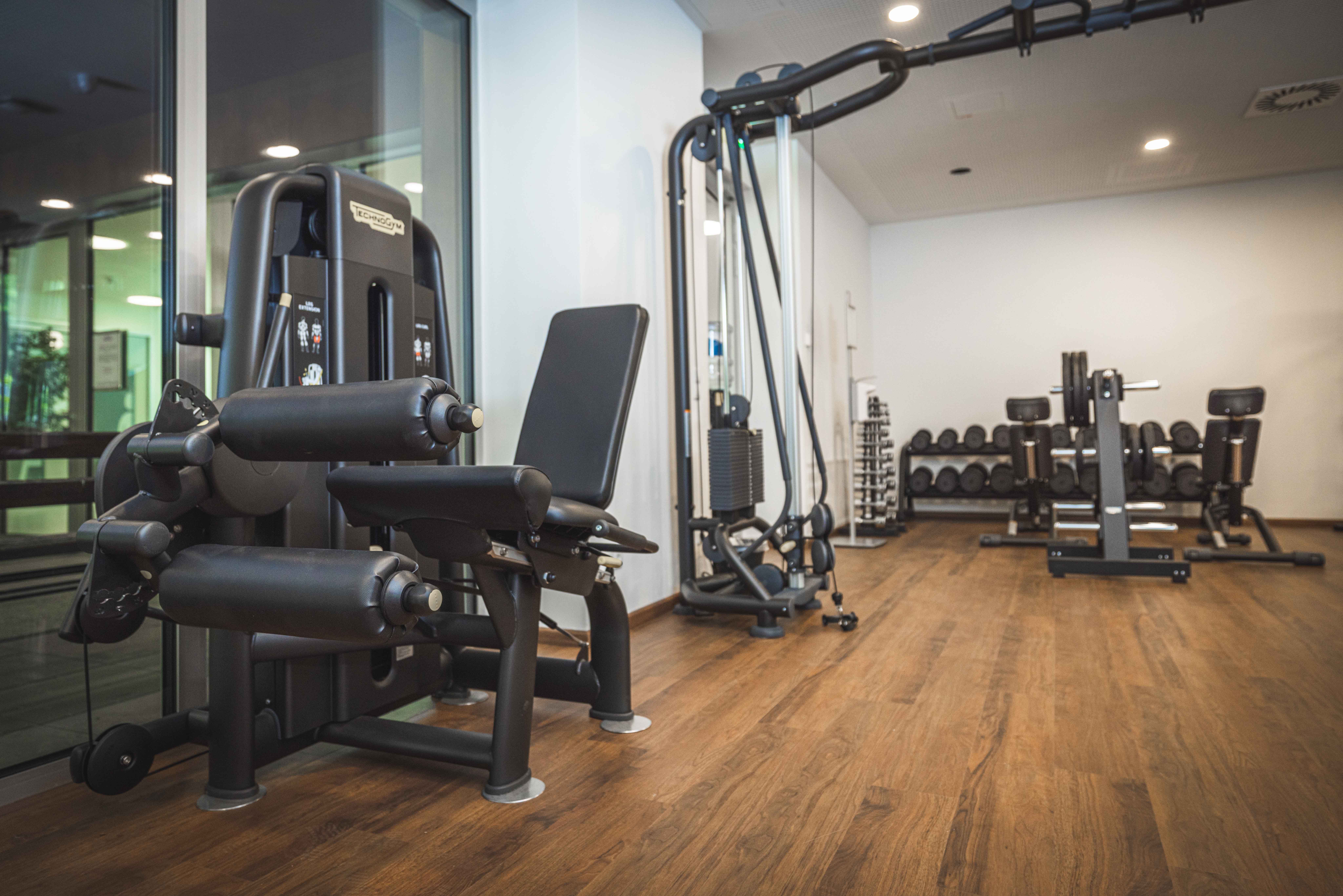 Fitnessraum im Schloss Haindorf mit modernen Kraftgeräten, Hanteln und Holzfußboden; keine Personen zu sehen.