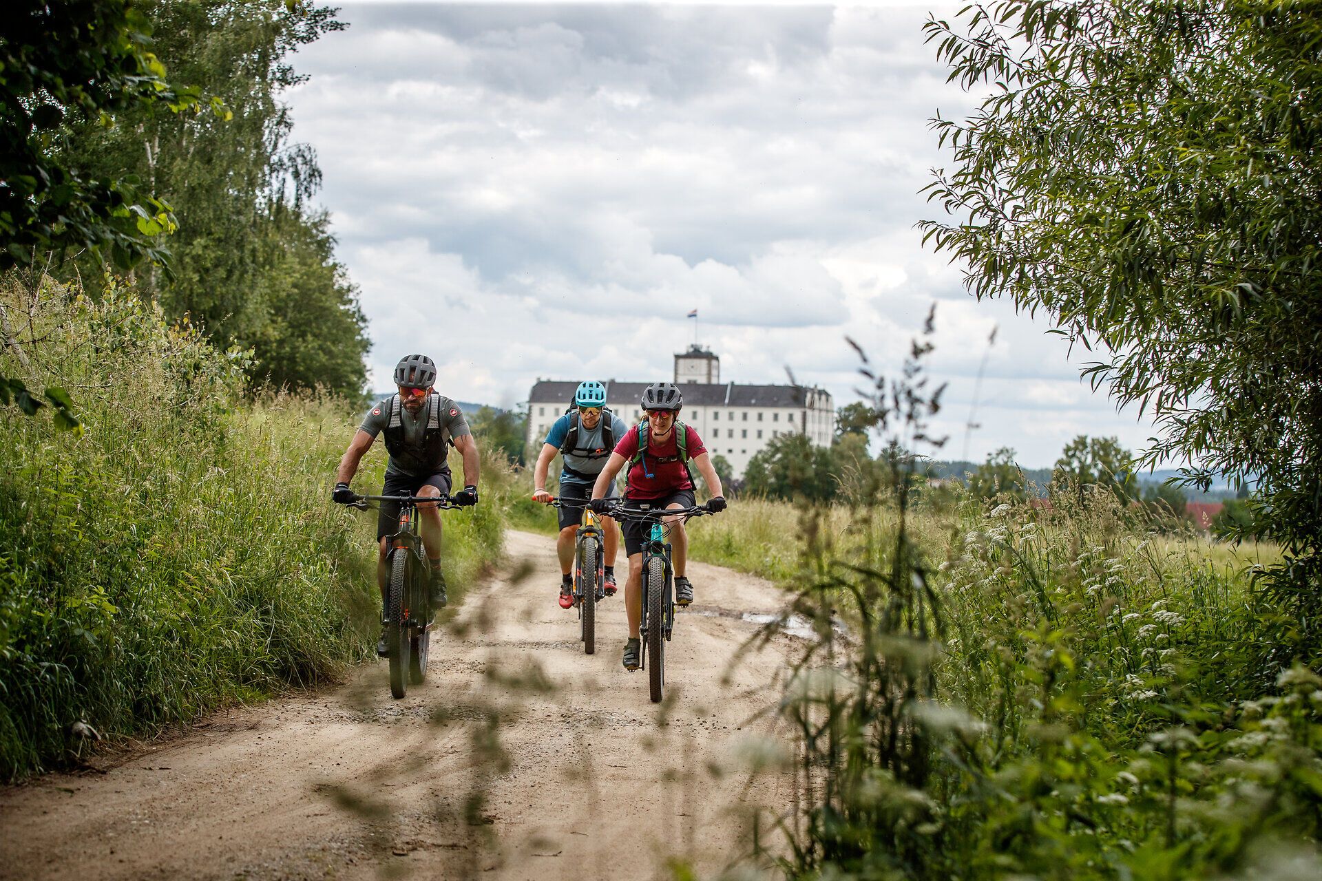 Drei Mountainbiker gleiten über einen schmalen, staubigen Pfad, umgeben von üppigem Grün und sanften Hügeln. Die frische Bergluft und die atemberaubende Landschaft laden zu einem unvergesslichen Abenteuer ein. Hier, wo Natur und Sport aufeinandertreffen, wird jeder Moment zum Erlebnis.