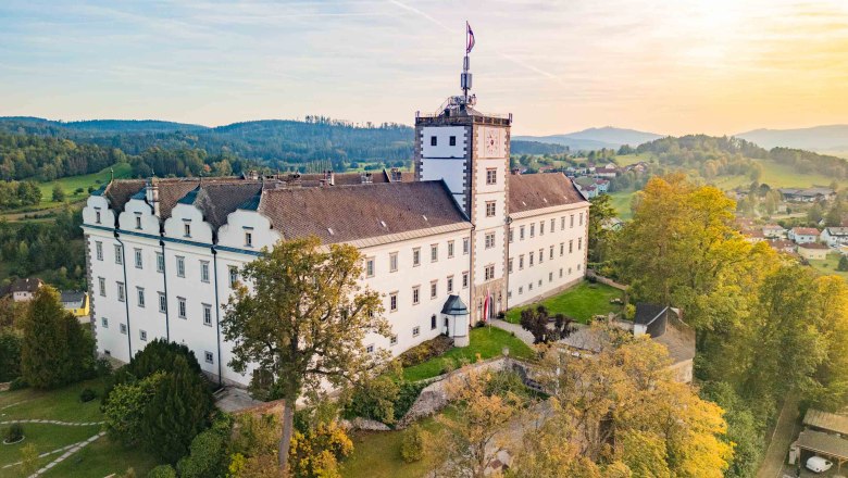 Luftaufnahme von Schloss Weitra in &Ouml;sterreich bei Sonnenuntergang, umgeben von gr&uuml;ner Landschaft und B&auml;umen.