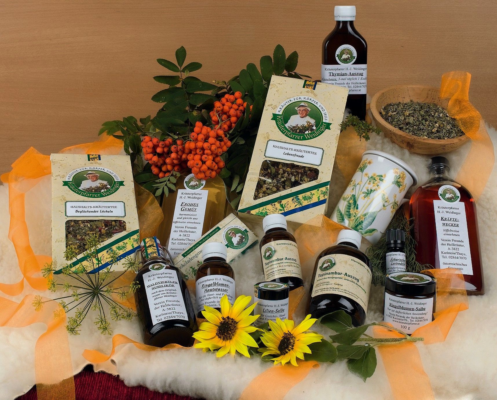 Verschiedene Kräuterprodukte von Kräuterpfarrer Weidinger, umgeben von Blumen und Beeren.