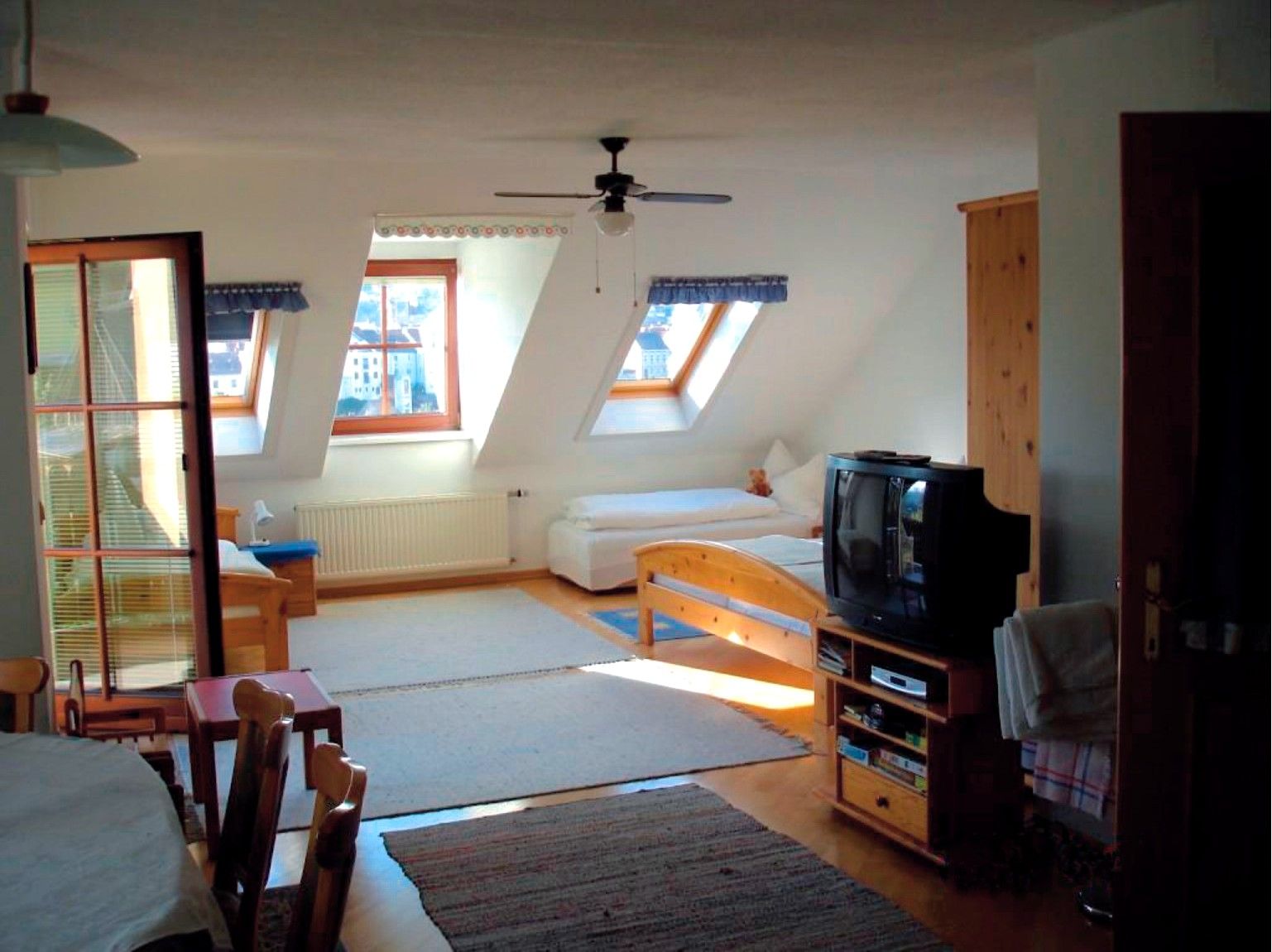 Innenansicht eines gemütlichen Dachgeschosszimmers mit Holzmöbeln, zwei Betten, einem Fernseher und Dachfenstern.