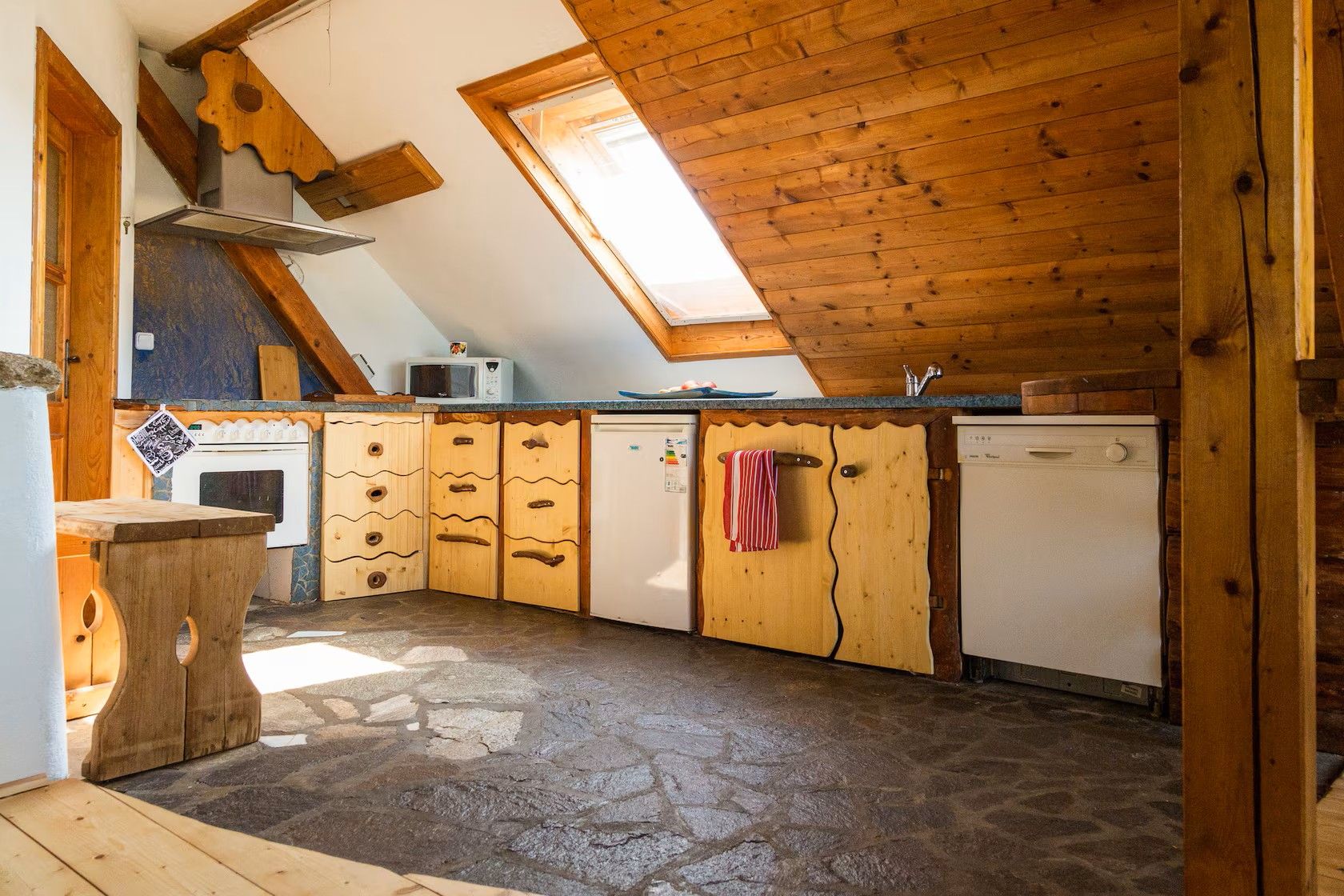 Rustikale Dachgeschossküche mit Holzverkleidung, Schrägdach, Dachfenster, Herd, Kühlschrank und Geschirrspüler.