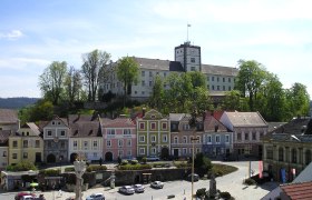 Schloss Weitra überblickt den Marktplatz mit bunten Häusern und einer Statue in Weitra, Österreich.