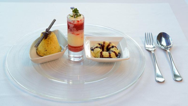 Three desserts on a plate: a cake, a layered dessert in a glass and a small cake ring, with cutlery next to it.