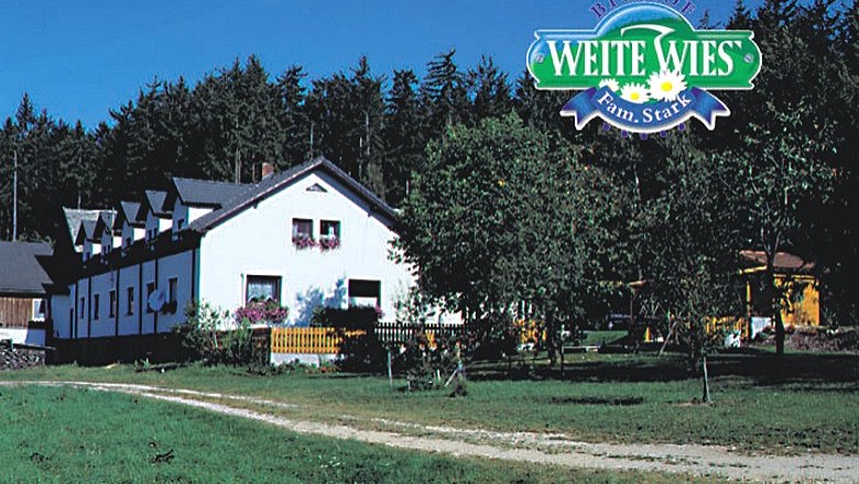 Ein wei&szlig;es Bauernhaus mit Blumen vor einem Wald, dar&uuml;ber das Logo 'Biohof Weite Wies Fam. Stark'.