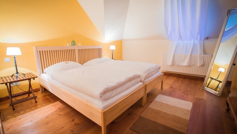 Gemütliches Schlafzimmer mit Doppelbett, Holzboden, gelber Wand und großem Spiegel.